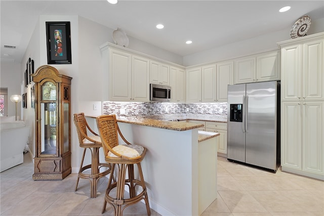 kitchen with light stone counters, kitchen peninsula, a breakfast bar, white cabinetry, and appliances with stainless steel finishes