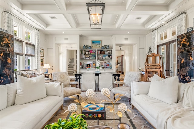 living room with coffered ceiling, ornamental molding, a fireplace, beam ceiling, and a chandelier