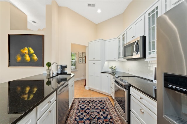 kitchen with appliances with stainless steel finishes, sink, light tile patterned floors, dark stone countertops, and white cabinets