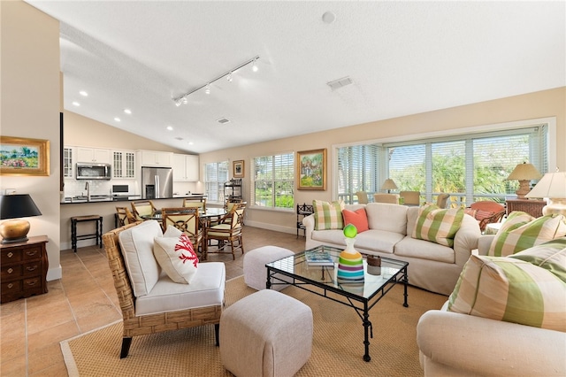 living room featuring a textured ceiling, light tile patterned floors, rail lighting, and vaulted ceiling