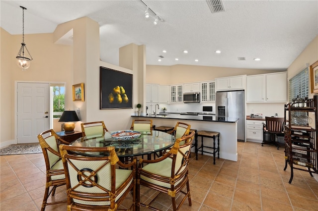 tiled dining space with a textured ceiling, sink, and high vaulted ceiling