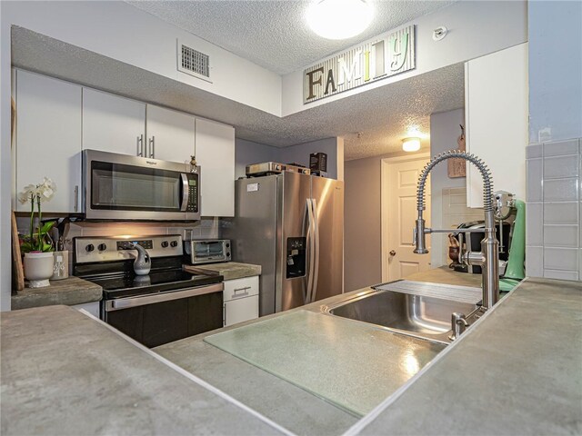 kitchen featuring a textured ceiling, appliances with stainless steel finishes, sink, and white cabinets