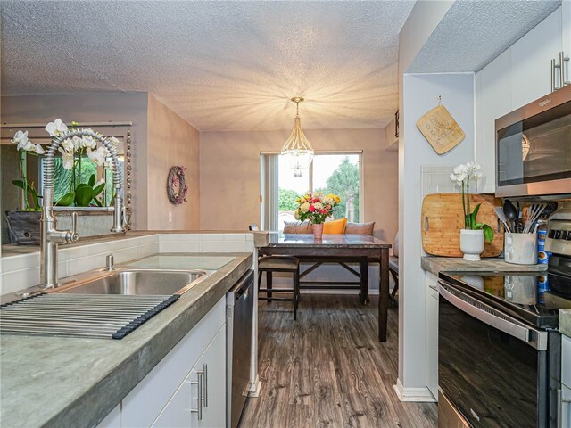 kitchen featuring white cabinetry, appliances with stainless steel finishes, a textured ceiling, hanging light fixtures, and dark wood-type flooring