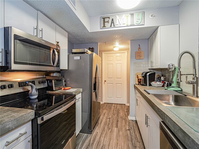 kitchen featuring white cabinetry, appliances with stainless steel finishes, a textured ceiling, light wood-type flooring, and sink