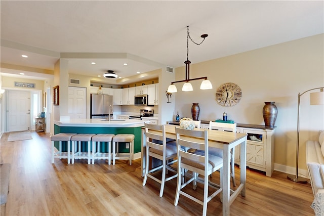 kitchen with stainless steel appliances, sink, pendant lighting, white cabinets, and light hardwood / wood-style floors