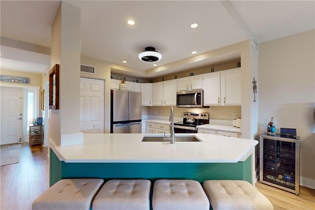 kitchen with a breakfast bar, stainless steel appliances, white cabinetry, and beverage cooler