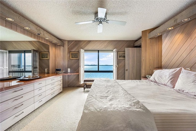 carpeted bedroom with a textured ceiling, ceiling fan, a water view, and wood walls