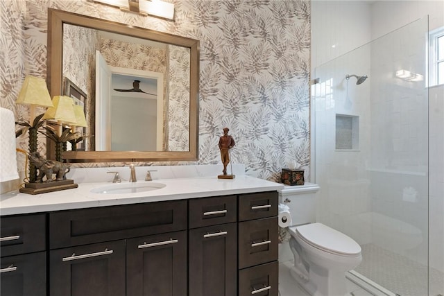 bathroom with toilet, ceiling fan, a tile shower, and vanity