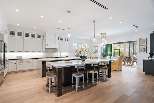 kitchen with a spacious island, hanging light fixtures, white cabinets, and light wood-type flooring