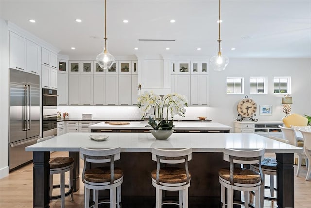 kitchen featuring stainless steel appliances, white cabinetry, a large island, and decorative light fixtures