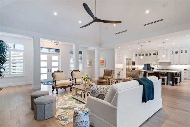 living room with ceiling fan, french doors, a high ceiling, and light hardwood / wood-style floors