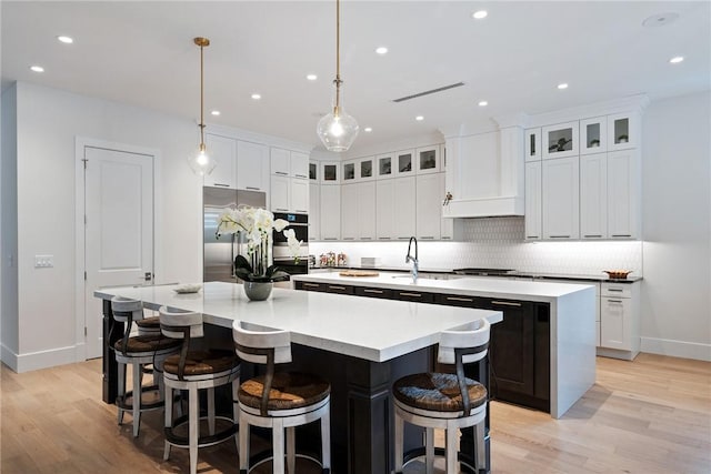 kitchen featuring white cabinetry, appliances with stainless steel finishes, a kitchen island with sink, custom range hood, and pendant lighting