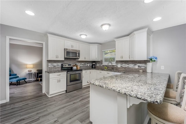 kitchen with a kitchen breakfast bar, stainless steel appliances, a peninsula, and white cabinets