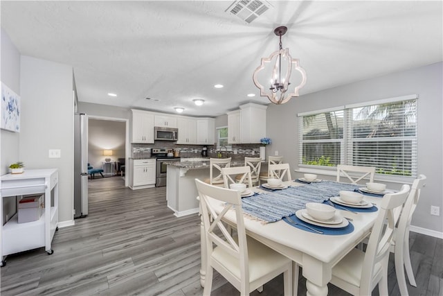 dining area featuring baseboards, visible vents, light wood finished floors, and an inviting chandelier