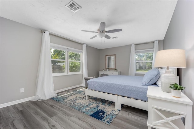 bedroom featuring ceiling fan, visible vents, baseboards, and wood finished floors