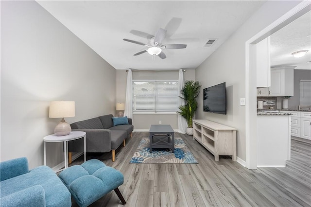 living room featuring ceiling fan, light wood-style flooring, visible vents, and baseboards