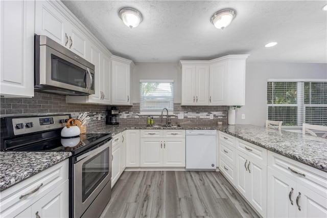 kitchen featuring tasteful backsplash, white cabinets, appliances with stainless steel finishes, light wood-type flooring, and a sink