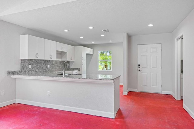 kitchen with kitchen peninsula, tasteful backsplash, light colored carpet, sink, and white cabinetry