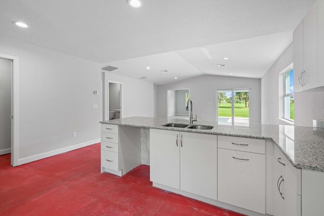 kitchen featuring white cabinets, sink, vaulted ceiling, carpet flooring, and light stone counters