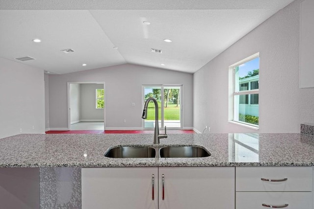 kitchen featuring white cabinets, light stone counters, sink, and vaulted ceiling