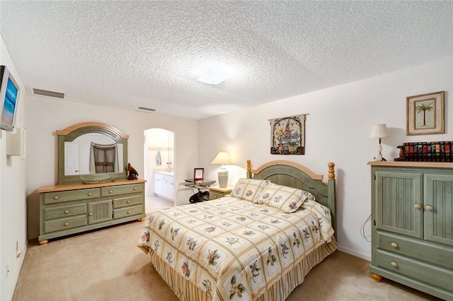 bedroom with light carpet, ensuite bath, and a textured ceiling