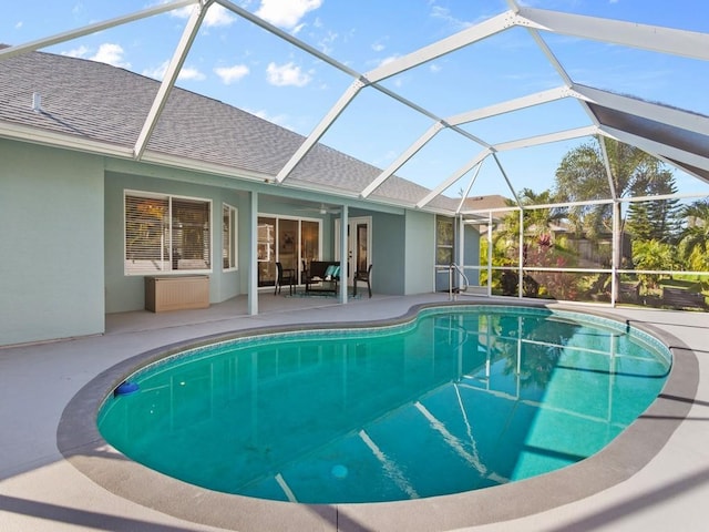 view of swimming pool featuring glass enclosure, ceiling fan, and a patio area