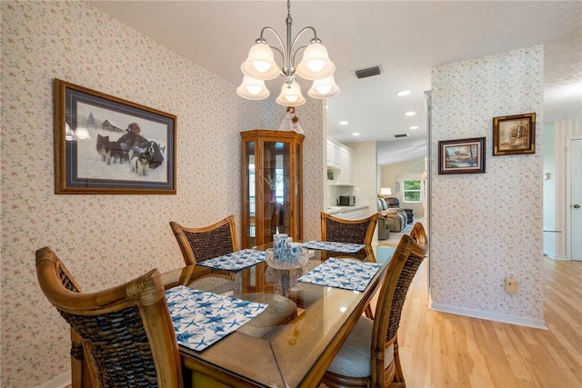 dining room with light wood-type flooring, baseboards, an inviting chandelier, and wallpapered walls