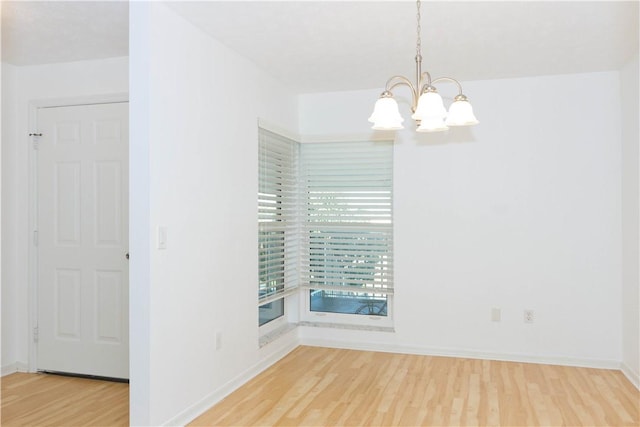 spare room featuring a chandelier, baseboards, and wood finished floors