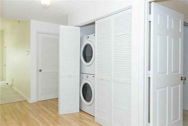 laundry room featuring baseboards, stacked washer / dryer, laundry area, and light wood-style floors