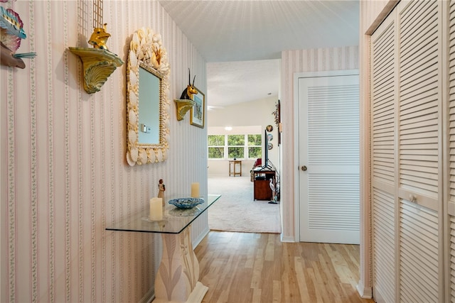 hall featuring a textured ceiling, lofted ceiling, and light wood-type flooring