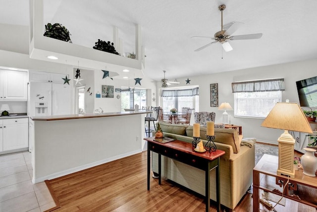 living area with light wood finished floors, vaulted ceiling, baseboards, and ceiling fan