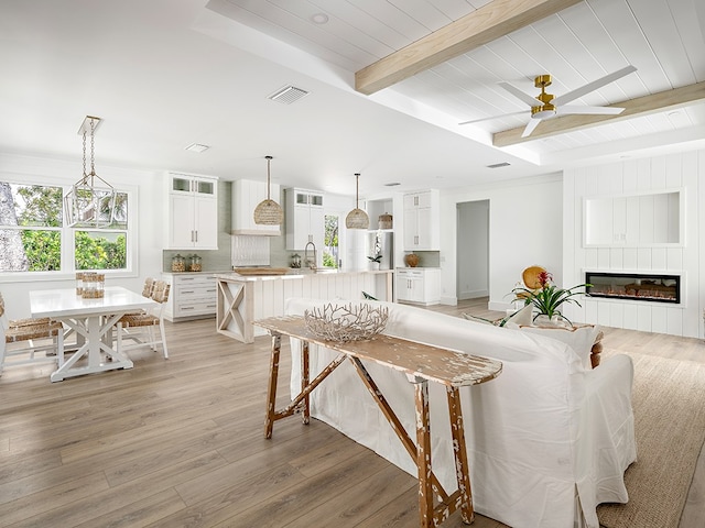 living room with light hardwood / wood-style floors, sink, beamed ceiling, ceiling fan, and a fireplace