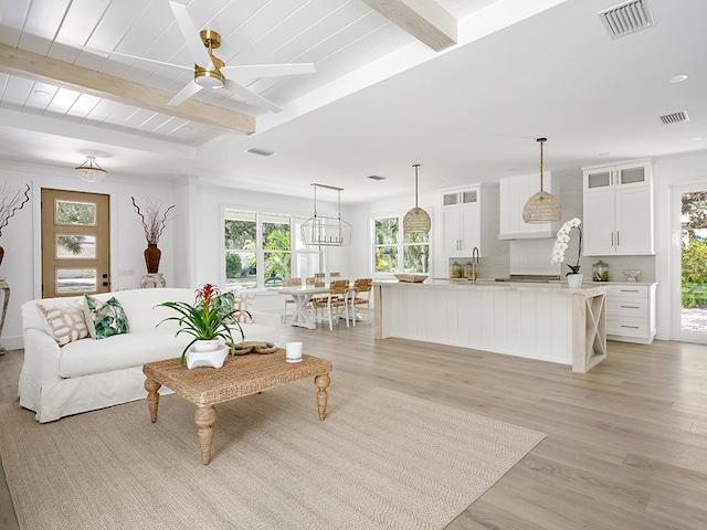 living room featuring beamed ceiling, ceiling fan with notable chandelier, sink, and light hardwood / wood-style flooring