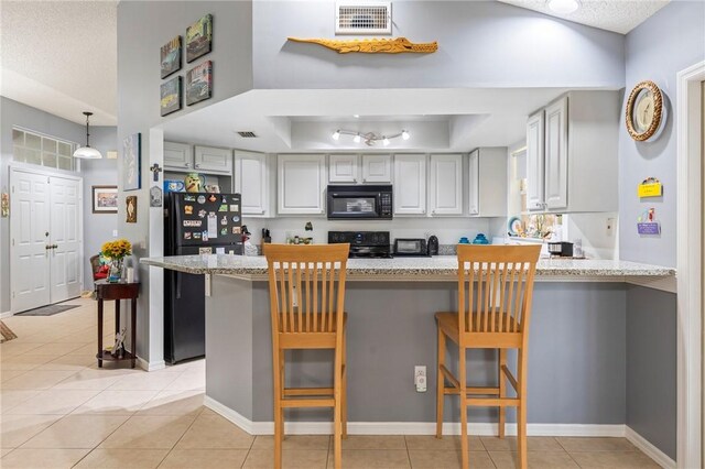 881 Foster Ave, Sebastian, FL 32958 - kitchen featuring black appliances, a peninsula, light tile patterned floors, light stone counters, and a tray ceiling