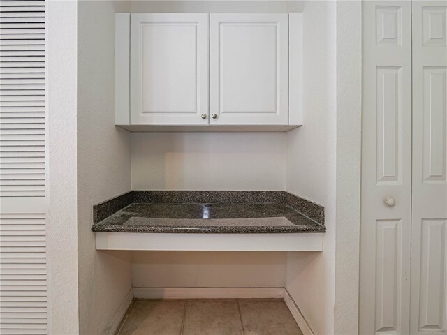 interior space with white cabinetry, built in desk, dark stone counters, and light tile patterned flooring