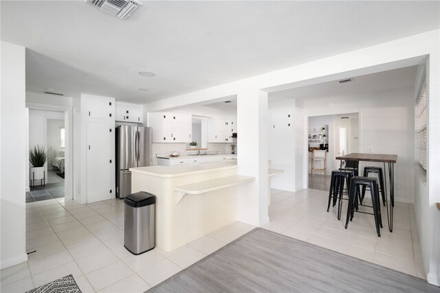 kitchen featuring kitchen peninsula, stainless steel refrigerator, light tile patterned floors, a breakfast bar area, and white cabinets