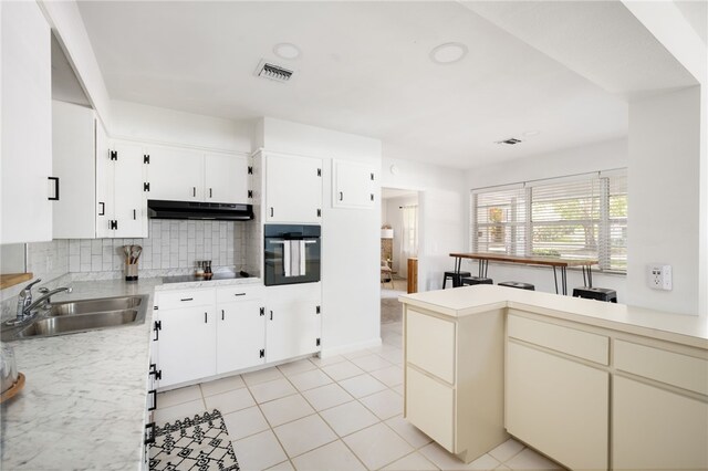 kitchen with tasteful backsplash, black appliances, sink, light tile patterned flooring, and white cabinetry