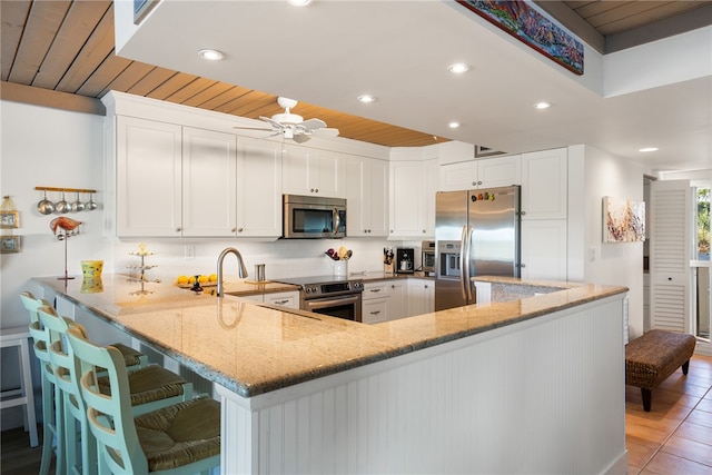 kitchen featuring wooden ceiling, light stone counters, kitchen peninsula, white cabinets, and appliances with stainless steel finishes