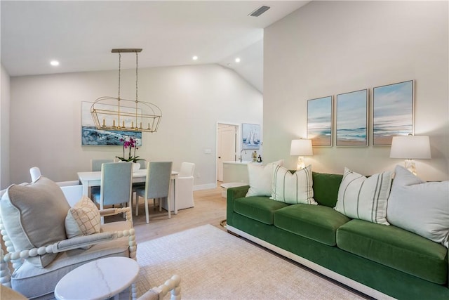 living room with a notable chandelier, high vaulted ceiling, and light hardwood / wood-style floors