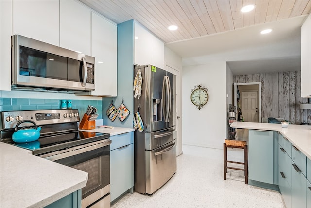 kitchen with backsplash, white cabinets, blue cabinetry, and stainless steel appliances