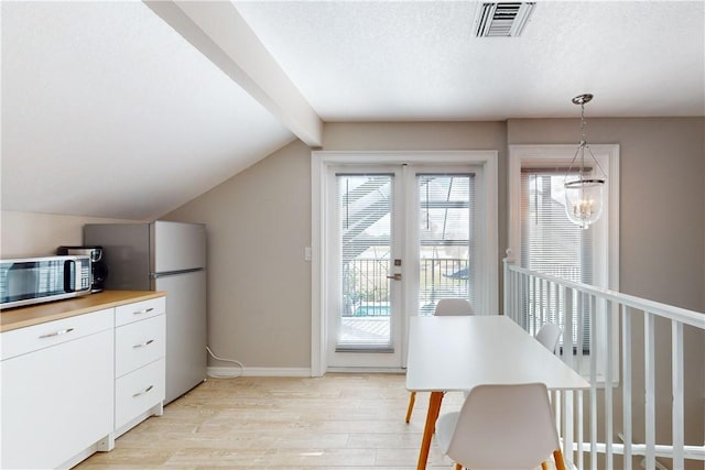 kitchen with appliances with stainless steel finishes, pendant lighting, lofted ceiling with beams, light hardwood / wood-style flooring, and white cabinetry