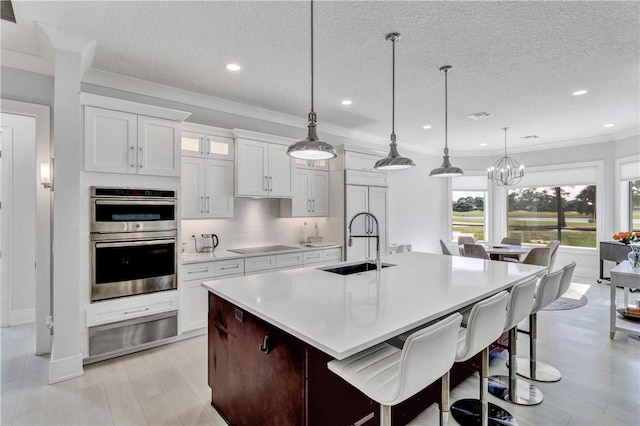 kitchen with sink, white cabinets, an island with sink, and decorative light fixtures