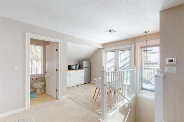 interior space with light carpet, a textured ceiling, a wealth of natural light, and a notable chandelier