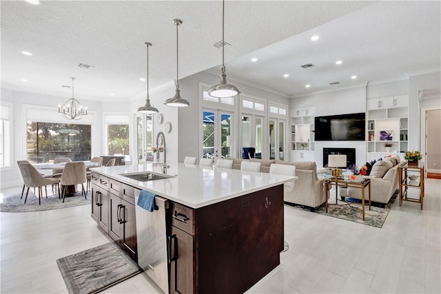 kitchen featuring sink, stainless steel dishwasher, pendant lighting, a textured ceiling, and a center island with sink