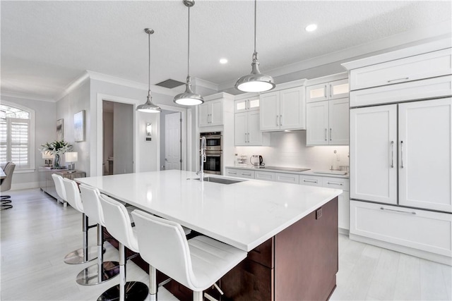 kitchen with a kitchen bar, ornamental molding, pendant lighting, a center island with sink, and white cabinets