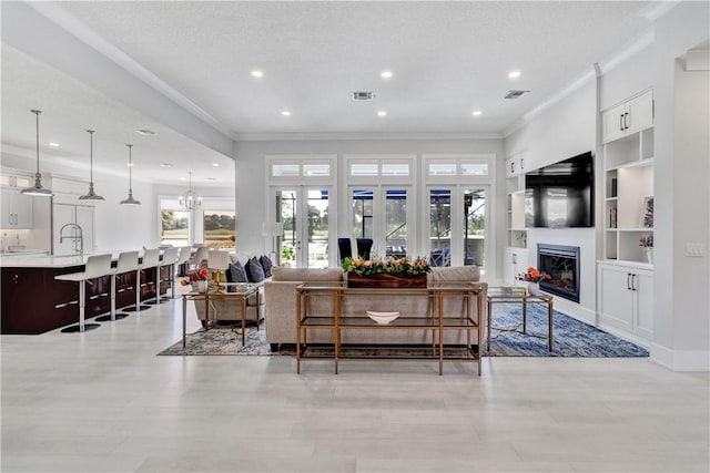 living room with french doors, a textured ceiling, crown molding, sink, and a notable chandelier