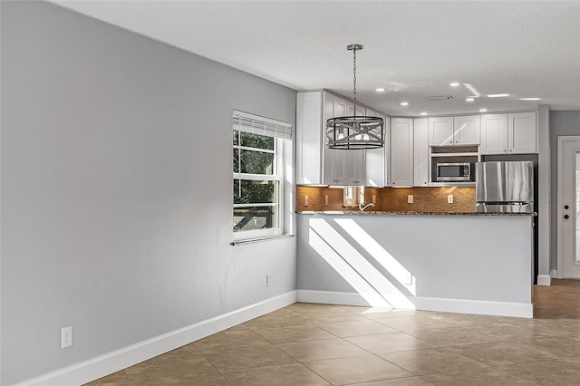 kitchen featuring appliances with stainless steel finishes, a notable chandelier, hanging light fixtures, white cabinets, and dark stone countertops