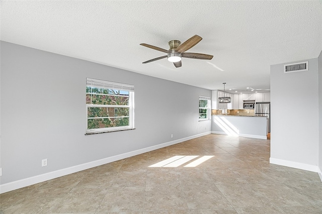 unfurnished living room with ceiling fan, a healthy amount of sunlight, and a textured ceiling