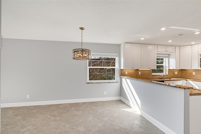 kitchen with dark stone counters, white cabinetry, decorative light fixtures, and kitchen peninsula