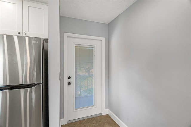 kitchen with tile patterned floors, a textured ceiling, stainless steel refrigerator, and white cabinets